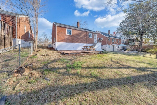 rear view of house with brick siding, fence, entry steps, a lawn, and a chimney