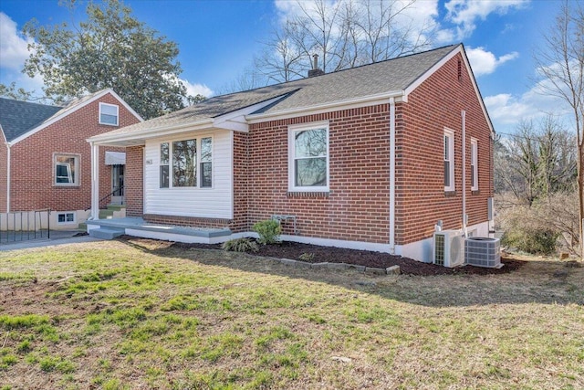 view of front facade featuring a front lawn, cooling unit, brick siding, and a chimney