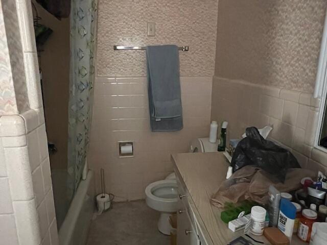 bathroom featuring wallpapered walls, tile walls, toilet, and wainscoting