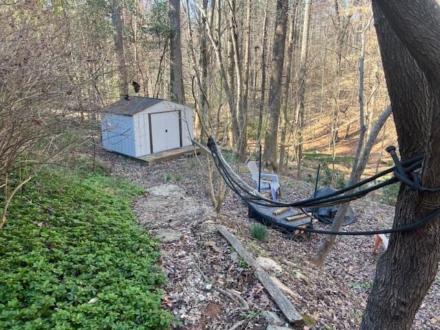 view of yard with an outbuilding, a wooded view, and a storage unit