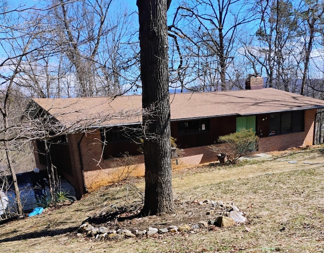 exterior space with a shingled roof, brick siding, and a chimney