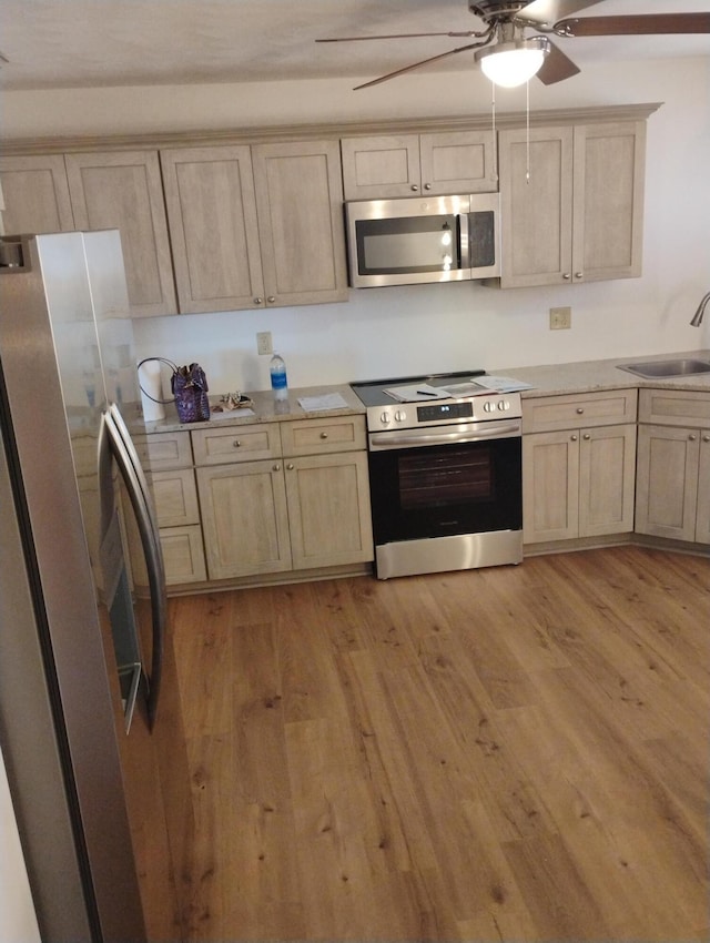 kitchen featuring light wood finished floors, appliances with stainless steel finishes, ceiling fan, and a sink