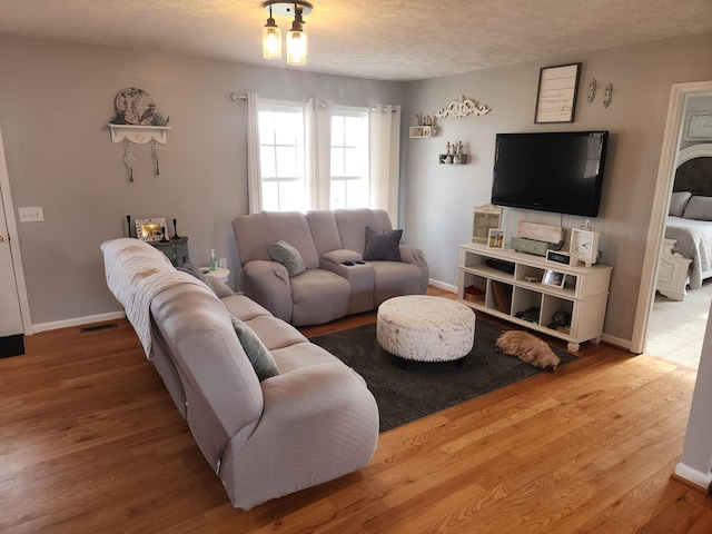 living room with visible vents, baseboards, a textured ceiling, and wood finished floors