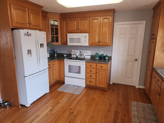 kitchen featuring dark countertops, white appliances, brown cabinetry, light wood finished floors, and glass insert cabinets