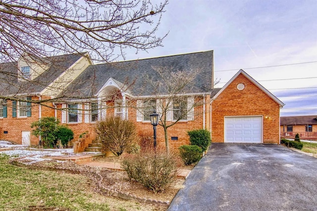 cape cod home featuring a garage, driveway, roof with shingles, crawl space, and brick siding