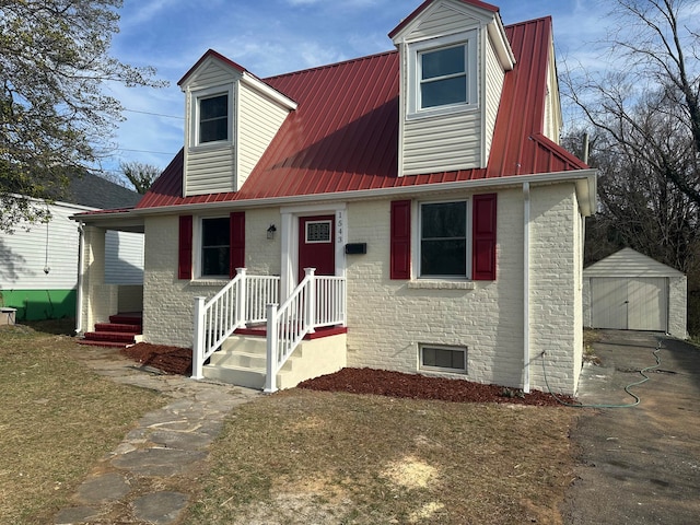 new england style home featuring metal roof, an outbuilding, brick siding, and a detached garage