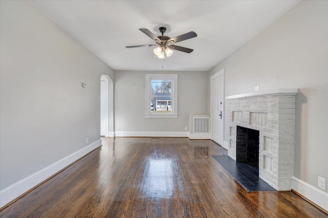 unfurnished living room with visible vents, a brick fireplace, baseboards, wood finished floors, and a ceiling fan