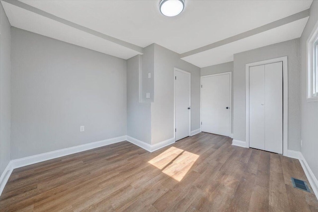 unfurnished bedroom featuring wood finished floors, visible vents, a closet, and baseboards