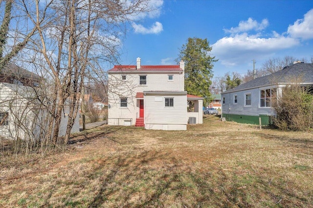 rear view of property with a lawn, a chimney, and entry steps