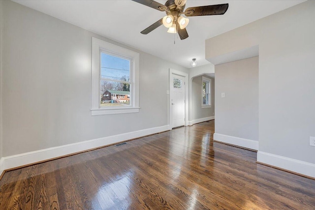 unfurnished room with visible vents, baseboards, wood finished floors, arched walkways, and a ceiling fan