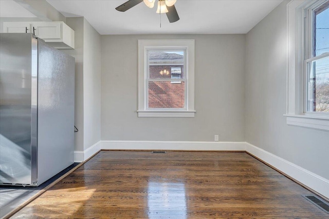 empty room with dark wood-style floors, visible vents, a ceiling fan, and baseboards
