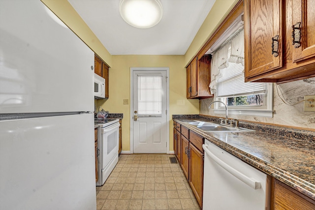 kitchen featuring dark countertops, decorative backsplash, brown cabinetry, white appliances, and a sink