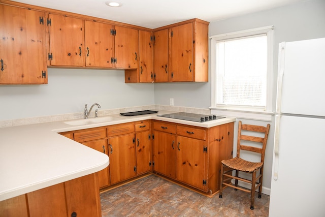 kitchen with light countertops, freestanding refrigerator, black electric stovetop, and a sink