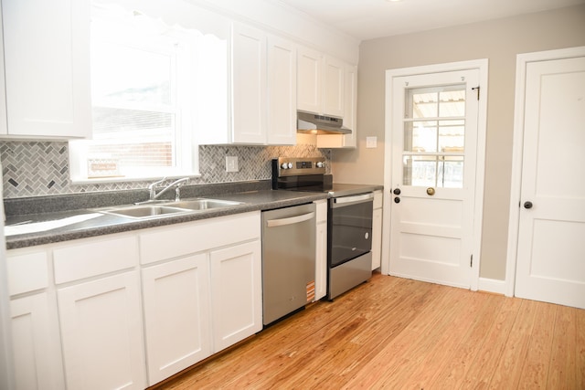 kitchen featuring a sink, stainless steel appliances, under cabinet range hood, dark countertops, and light wood-type flooring