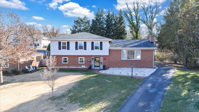 split level home with aphalt driveway, a chimney, a front yard, and brick siding