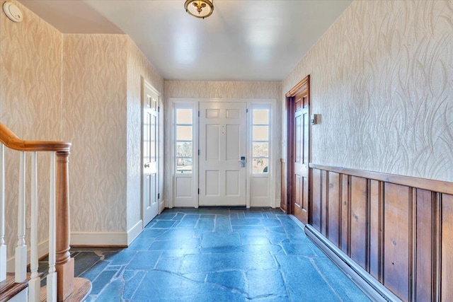 foyer entrance with stone tile floors, wallpapered walls, stairs, and baseboards