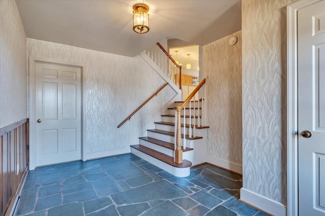 stairway with stone tile floors, wallpapered walls, and baseboards