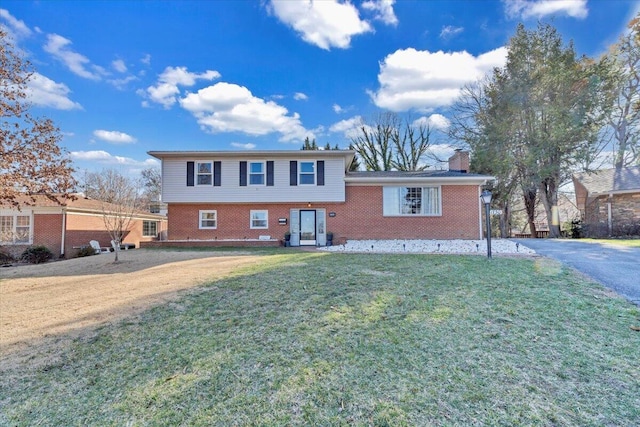 split level home with brick siding, a chimney, and a front yard