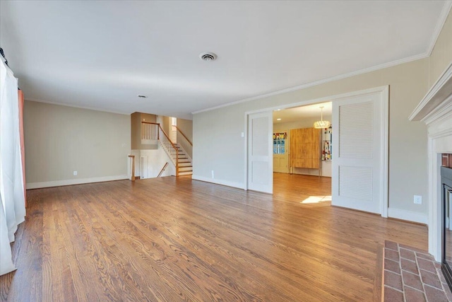 unfurnished living room with stairway, a fireplace with flush hearth, wood finished floors, and ornamental molding