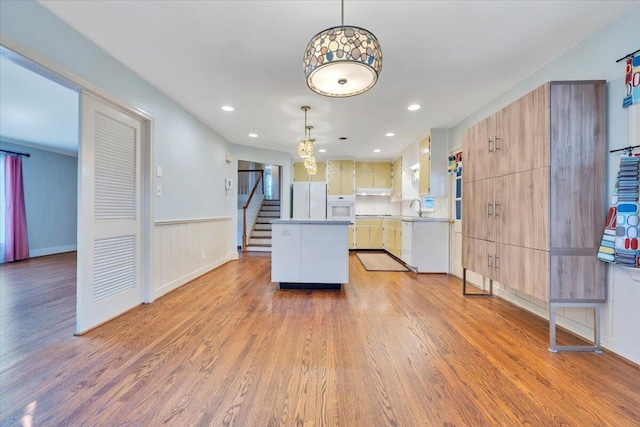 kitchen featuring white appliances, a kitchen island, a sink, hanging light fixtures, and light wood-type flooring