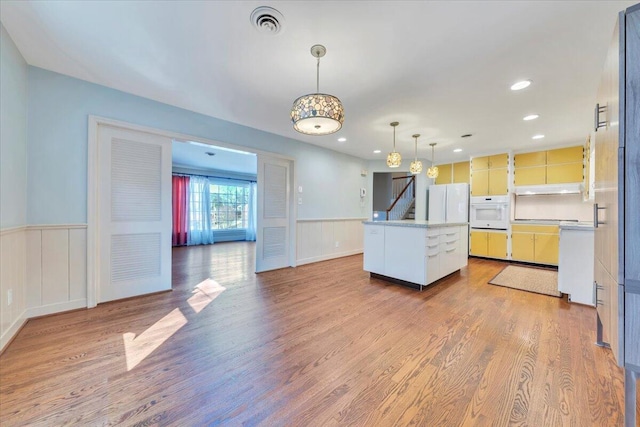 kitchen featuring a kitchen island, a wainscoted wall, light countertops, wood finished floors, and white oven