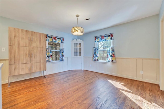 empty room featuring light wood finished floors, a wainscoted wall, and visible vents