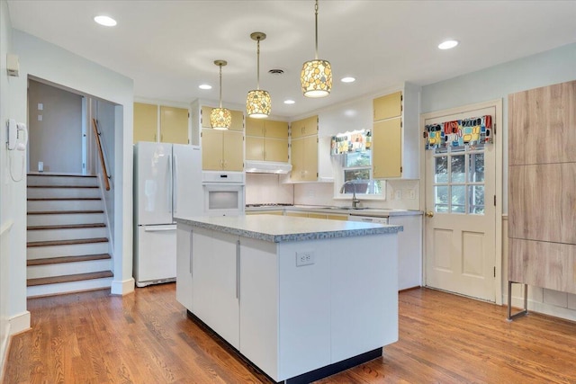 kitchen featuring white appliances, wood finished floors, a kitchen island, light countertops, and under cabinet range hood