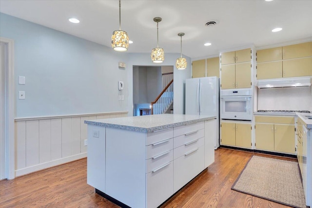 kitchen featuring under cabinet range hood, visible vents, white appliances, and cream cabinets