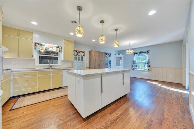 kitchen featuring a wainscoted wall, a sink, a kitchen island, white dishwasher, and light countertops