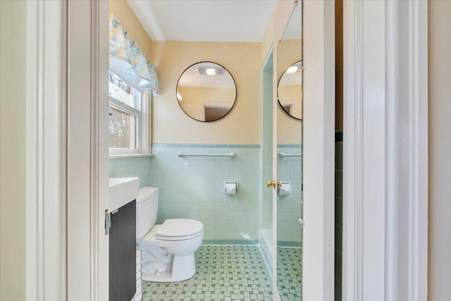 bathroom with wainscoting, vanity, toilet, and tile walls