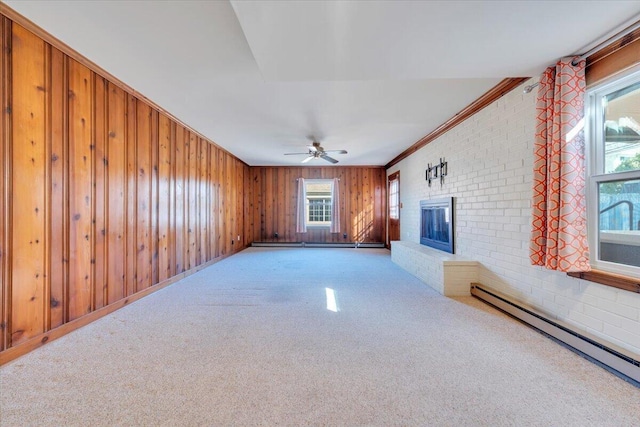 unfurnished living room with a brick fireplace, wood walls, carpet floors, a ceiling fan, and a baseboard radiator