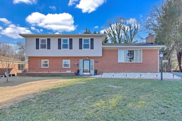 tri-level home with brick siding, a chimney, and a front yard