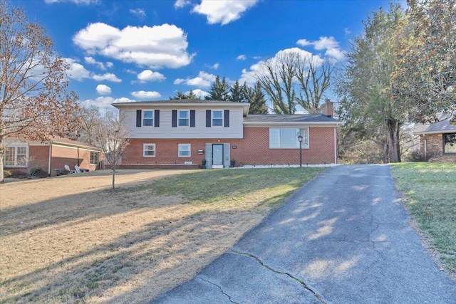 split level home featuring brick siding, driveway, a chimney, and a front lawn