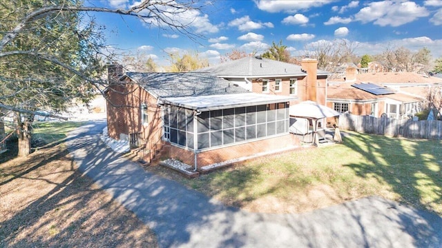 rear view of property with a lawn, fence, a sunroom, brick siding, and a chimney