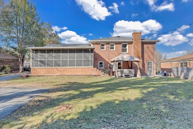 rear view of house with a yard, a sunroom, brick siding, a chimney, and a hot tub