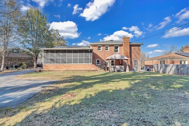 back of house with fence, a yard, a sunroom, brick siding, and a chimney