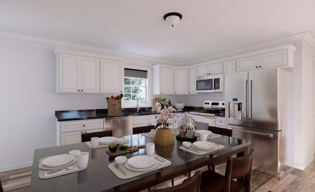 kitchen with a sink, dark countertops, appliances with stainless steel finishes, white cabinets, and light wood finished floors