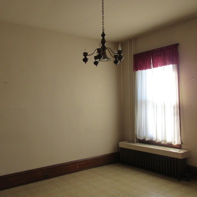 empty room with baseboards, a chandelier, and radiator heating unit