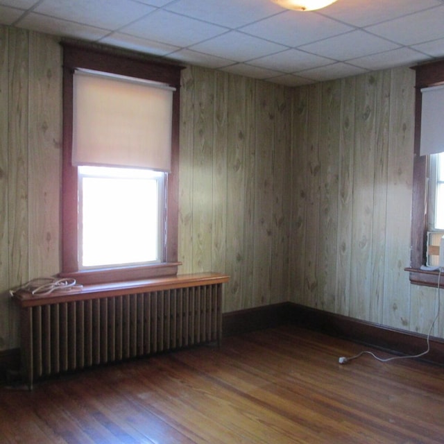 spare room with a drop ceiling, radiator, wooden walls, and wood finished floors