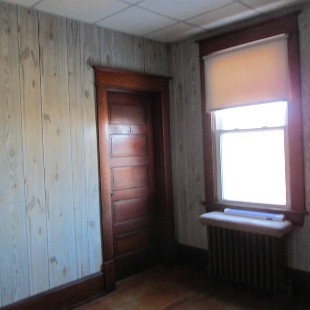 unfurnished bedroom with a drop ceiling, wood walls, and radiator heating unit