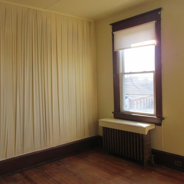 empty room with hardwood / wood-style floors, radiator heating unit, and baseboards