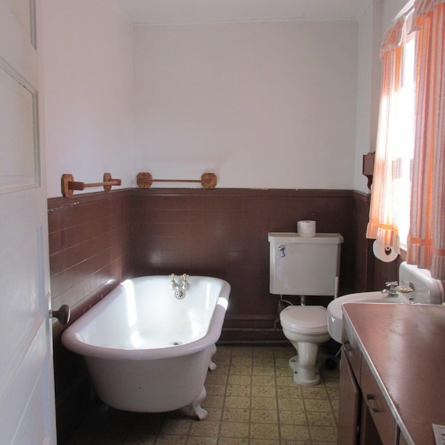 bathroom featuring a soaking tub, wainscoting, toilet, and a healthy amount of sunlight