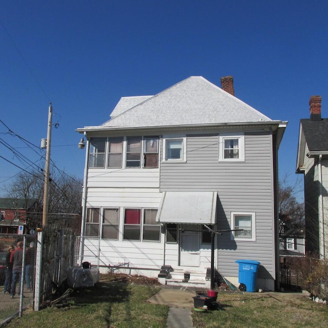 back of house featuring fence, roof with shingles, a yard, a chimney, and entry steps