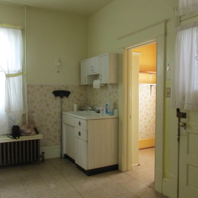 kitchen with radiator, wallpapered walls, baseboards, light countertops, and a sink