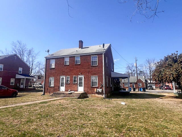 back of house featuring a lawn, brick siding, and a chimney