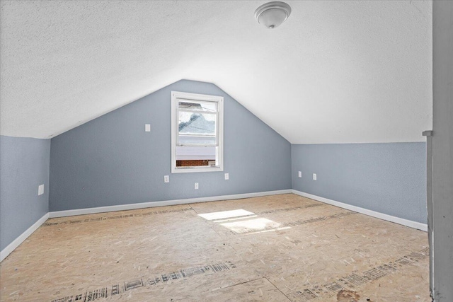 additional living space with a textured ceiling, baseboards, and vaulted ceiling