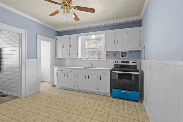 kitchen with a wainscoted wall, stainless steel electric range oven, light countertops, white cabinets, and a sink