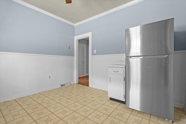 kitchen with visible vents, crown molding, a wainscoted wall, freestanding refrigerator, and white cabinets