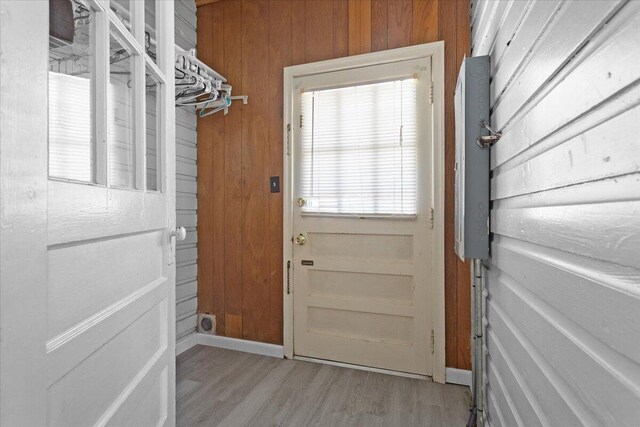 doorway featuring light wood-type flooring, baseboards, and wooden walls