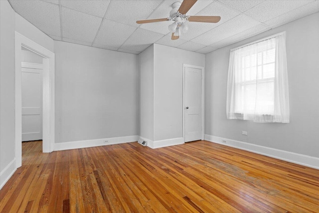 spare room with ceiling fan, a drop ceiling, baseboards, and hardwood / wood-style floors